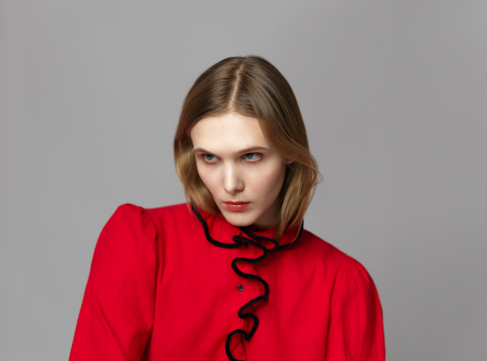Viktoria Yerchyk in roter Bluse mit schwarzer Rüschenkante, Nahaufnahme mit direktem Blick, Fashion-Strecke