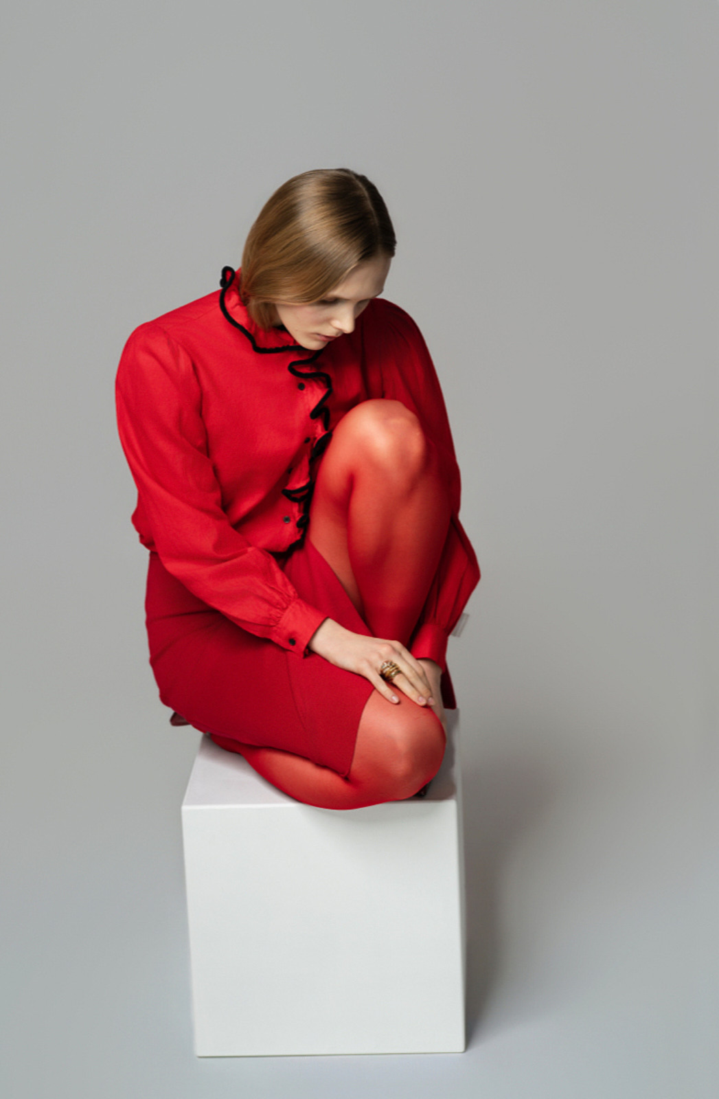 Viktoria Yerchyk in rotem Ensemble mit schwarzer Rüschenkante, auf einem Würfel sitzend, Fashion-Strecke
