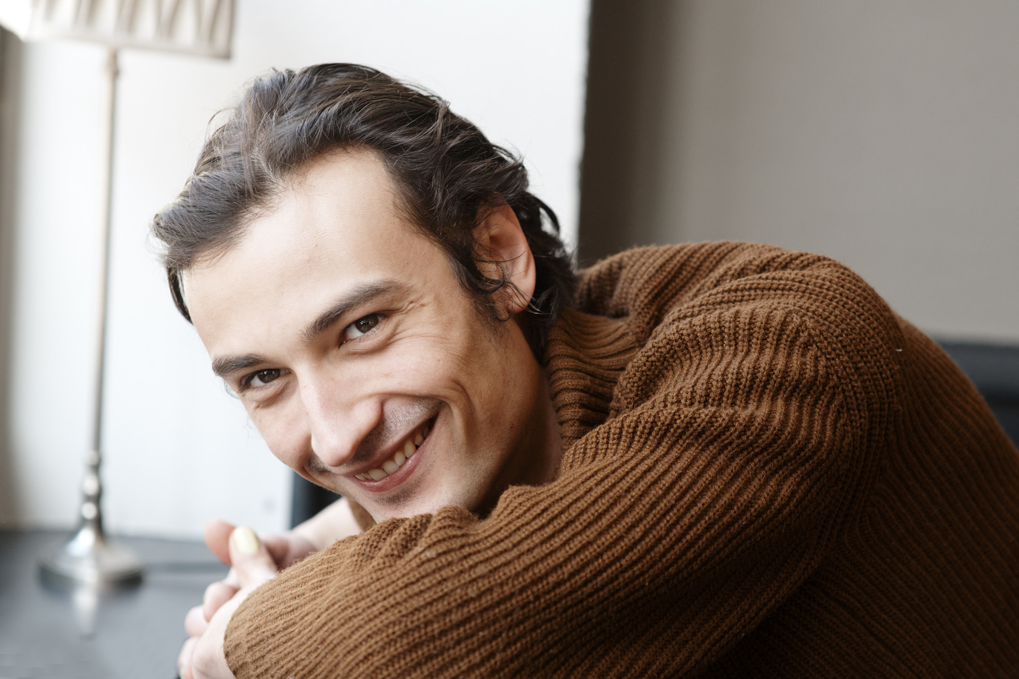 Schauspieler Jakob D'Aprile l&auml;chelnd, das Kinn auf den verschr&auml;nkten Armen im Strickpullover, Schauspielerportr&auml;t von Martina Thalhofer, Berlin