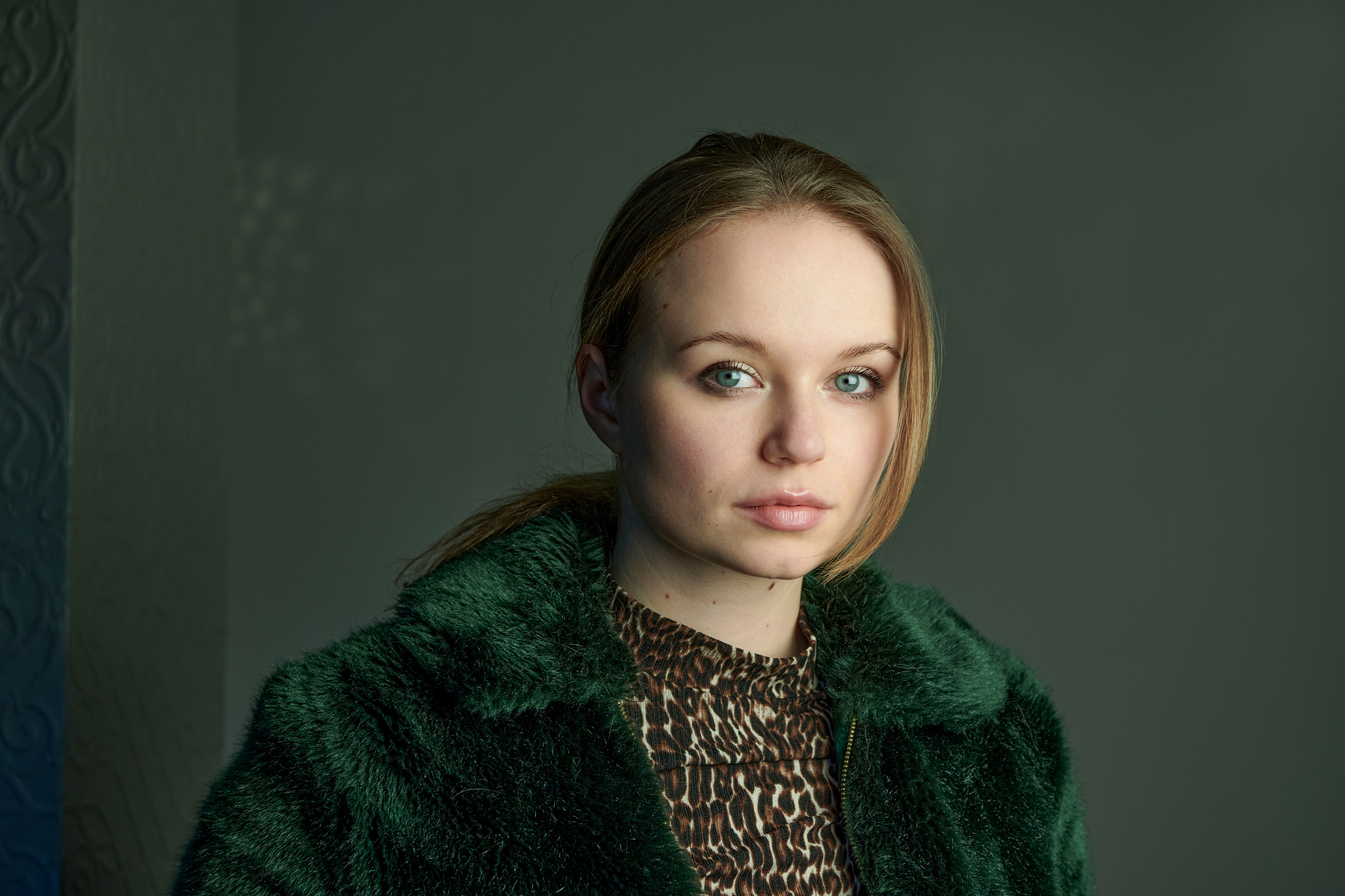 Larissa Sophie Römer in grüner Plüschjacke über einem Oberteil mit Leopardenmuster vor dunkelgrüner Wand
